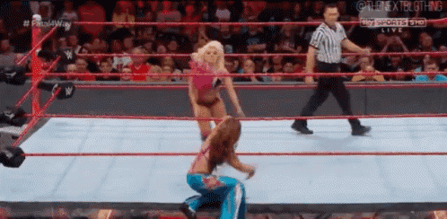 a woman is kneeling down in a wrestling ring while a referee looks on .