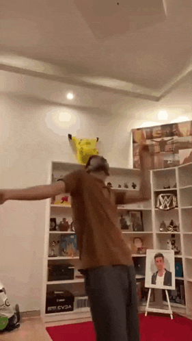 a man is dancing in a living room with a picture of a man on an easel in the background .