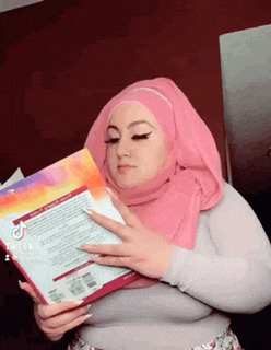 a woman wearing a pink hijab is holding a book in her hands .