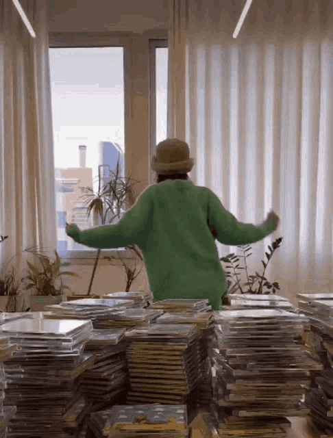 a person in a green sweater and hat is standing in front of a stack of cds