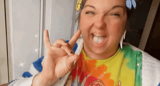 a woman wearing a tie dye shirt and ear buds is making a funny face with her tongue sticking out .