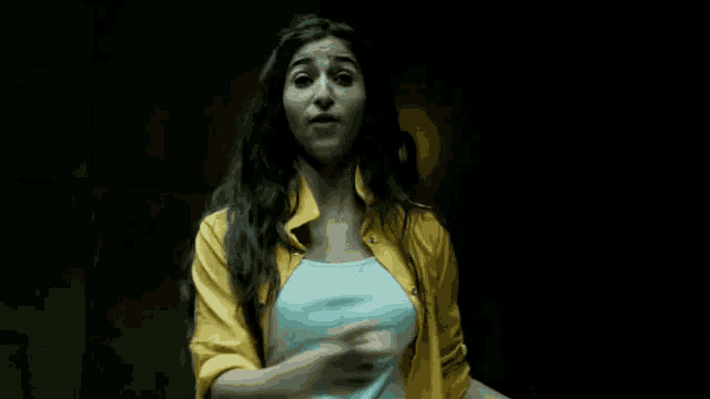 a woman wearing a yellow shirt and a white tank top is pointing at the camera .