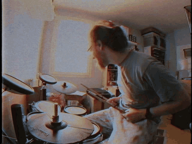a man in a gray shirt is playing a set of drums
