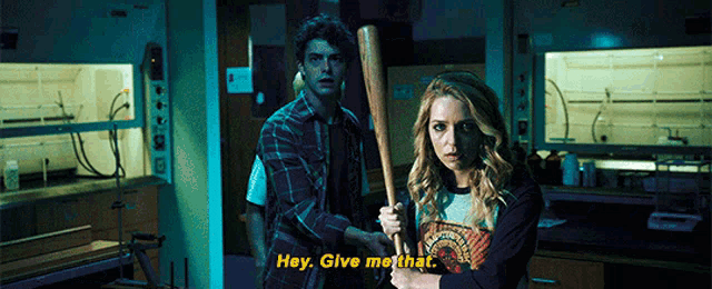 a man and a woman are holding a baseball bat in a dark room and the woman says hey give me that