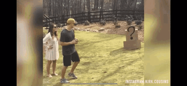 a man and woman are standing in front of a cardboard box with a question mark painted on it .