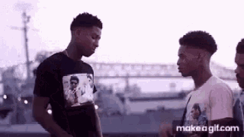 three young men are standing next to each other in front of a bridge and talking .