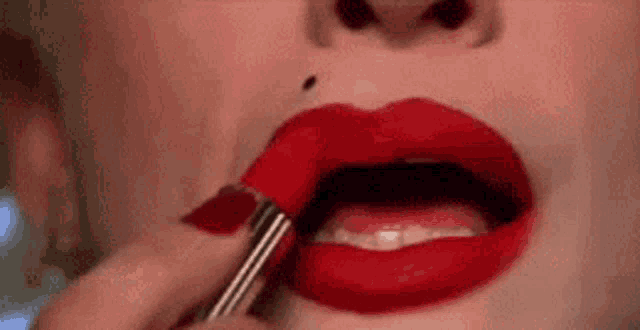 a woman is putting red lipstick on her lips .