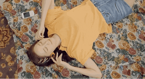 a woman laying on a floral blanket listening to music with headphones