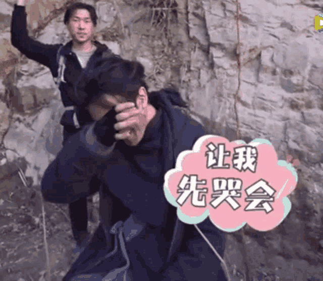 a man covering his face while another man stands behind him with chinese writing on a pink cloud