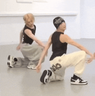 a man in a black tank top is squatting next to another man in white pants