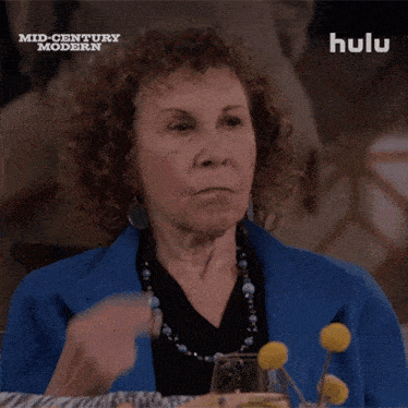 a woman in a blue jacket is sitting at a table with a hulu logo behind her