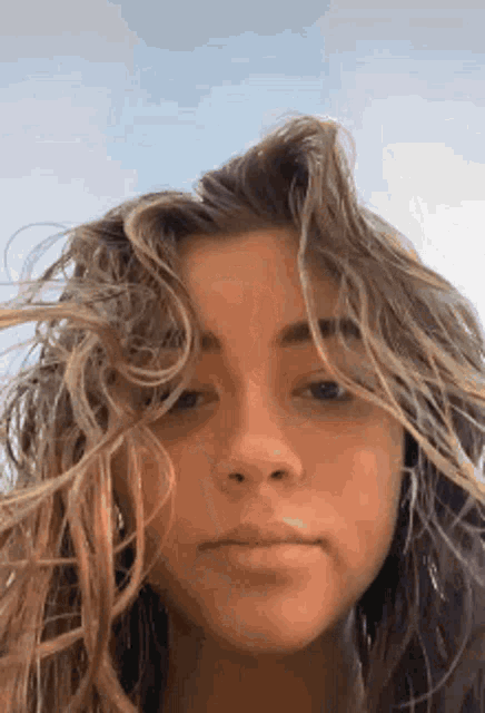 a close up of a woman 's face with her hair blowing in the wind and a blue sky in the background .