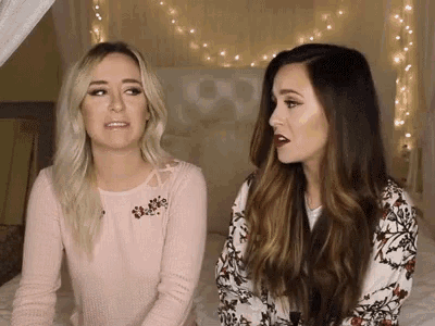 two women are sitting next to each other on a bed talking to each other .