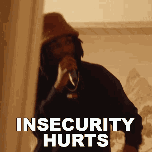 a man in a hat is singing into a microphone and the words insecurity hurts are on the screen .