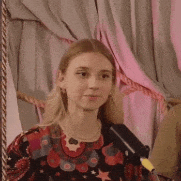 a woman stands in front of a microphone and a pink curtain