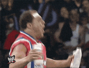 a man in a red , white and blue wrestling uniform is holding a piece of paper in front of a crowd .