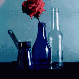 a blue bottle with a red rose in it sits next to a clear bottle