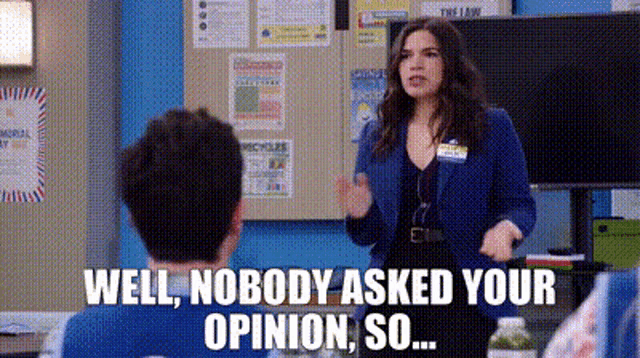 a woman in a blue jacket is standing in front of a man in a classroom and talking to him .