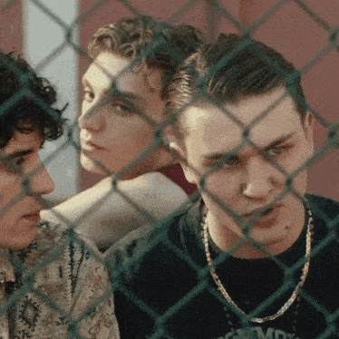 three young men are behind a chain link fence and one of them is wearing a shirt that says commd