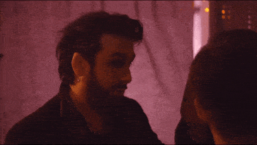 a man with a beard and ear piercings looks at another man