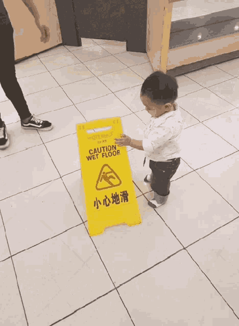 a child is standing next to a yellow sign that says caution wet floor