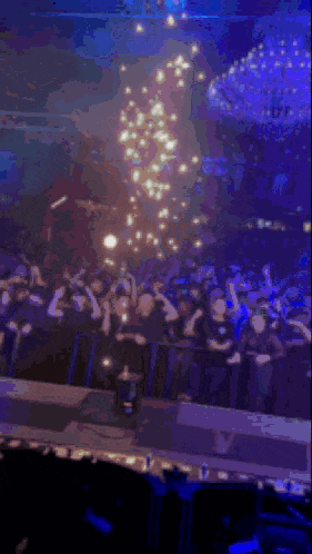 a blurry picture of a crowd at a concert with a large chandelier in the background