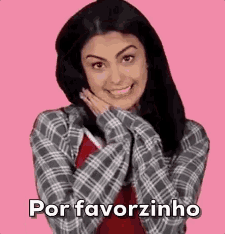 a woman in a plaid shirt is smiling and holding her hands to her face on a pink background .