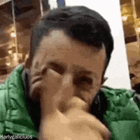 a man wearing a green jacket is covering his face with his hand .