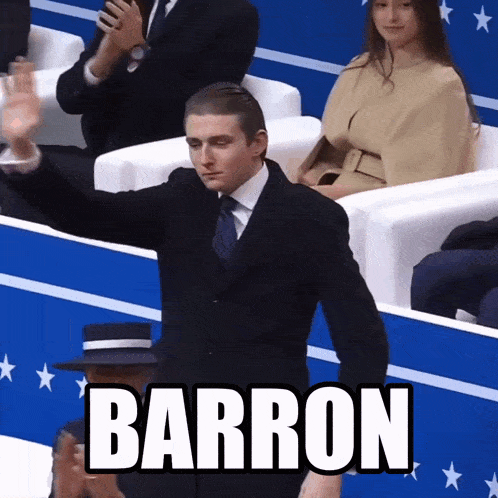 a man in a suit and tie stands in front of a crowd and the word barron is on the screen behind him