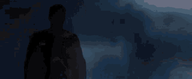 a man in a superman costume is standing in the dark with a red s on his chest .