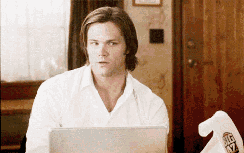 a man in a white shirt is sitting in front of a laptop with a big oz t-shirt on the table