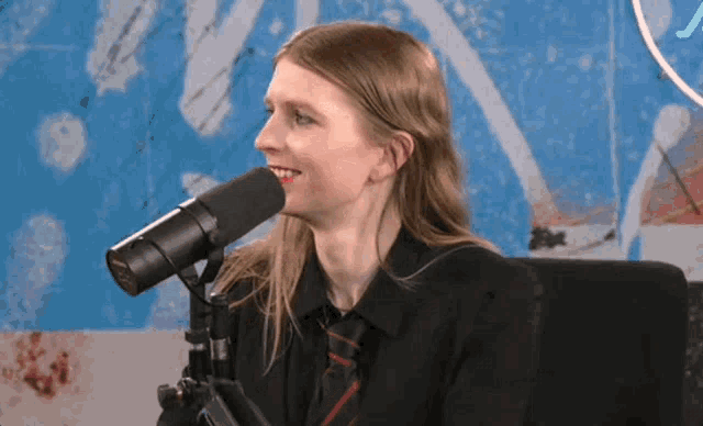 a woman with long hair is sitting in front of a microphone and smiling