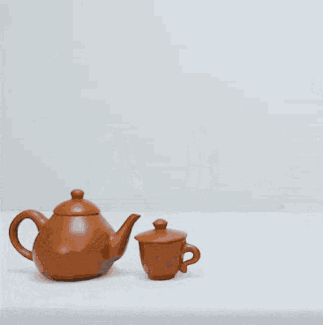 a woman wrapped in a white blanket looks at a teapot and cup on a table