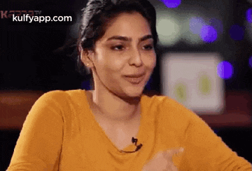 a woman in a yellow shirt is sitting at a table with a microphone in her mouth .