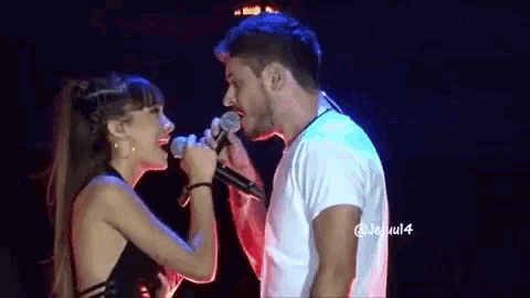 a man and a woman are singing into microphones on a stage and looking at each other .