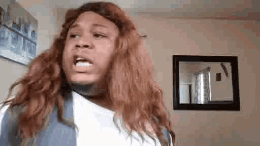 a woman with long red hair is making a funny face while standing in front of a mirror in a living room .