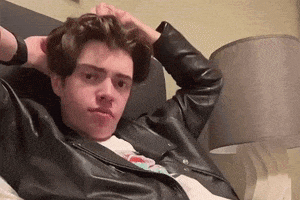 a young man in a leather jacket is laying on a bed and adjusting his hair .