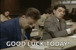 mr bean is sitting at a desk writing on a piece of paper and says `` good luck today ! ''