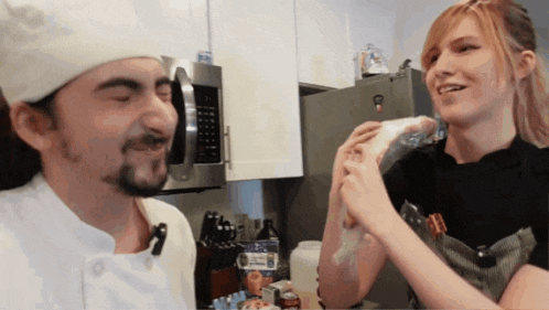 a man in a chef 's hat looks at a woman holding something