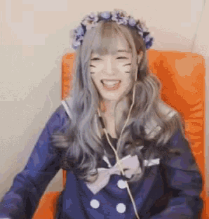 a girl with a flower crown on her head is sitting in a chair and smiling .
