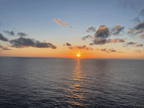the sun is setting over the ocean with a cloudy sky