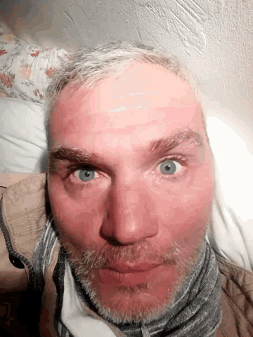 a man with a beard and blue eyes laying down