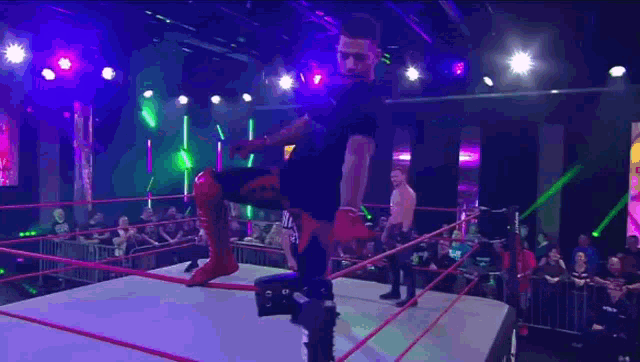 a wrestler is standing in a wrestling ring with a referee in front of a crowd .