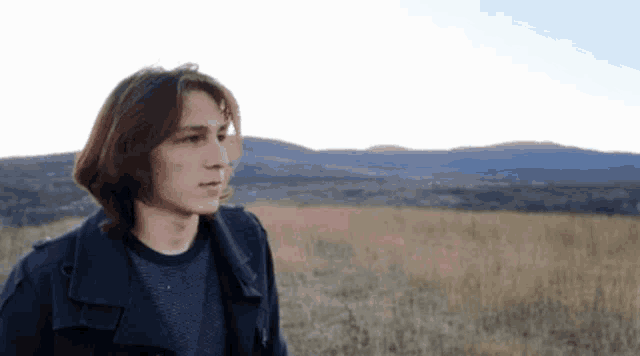 a young man standing in a field with a mountain in the background