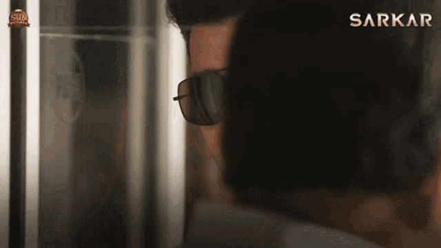 a man wearing sunglasses is standing in front of a screen that says sarkar