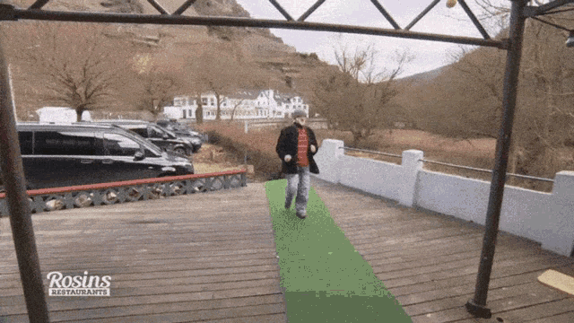 a man is walking on a green carpet with rosin 's restaurant in the background