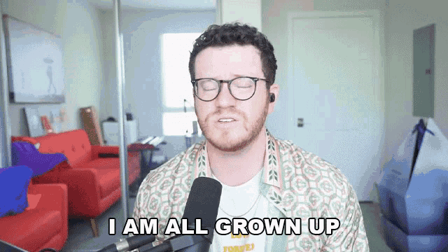 a man with glasses and a beard says i am all grown up in front of a microphone