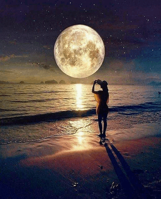 a woman standing on a beach taking a picture of the moon