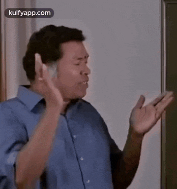a man in a blue shirt is standing in front of a blackboard and making a funny face .