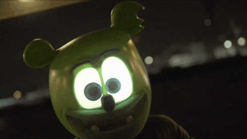 a green gummy bear with glowing eyes is being held by a person